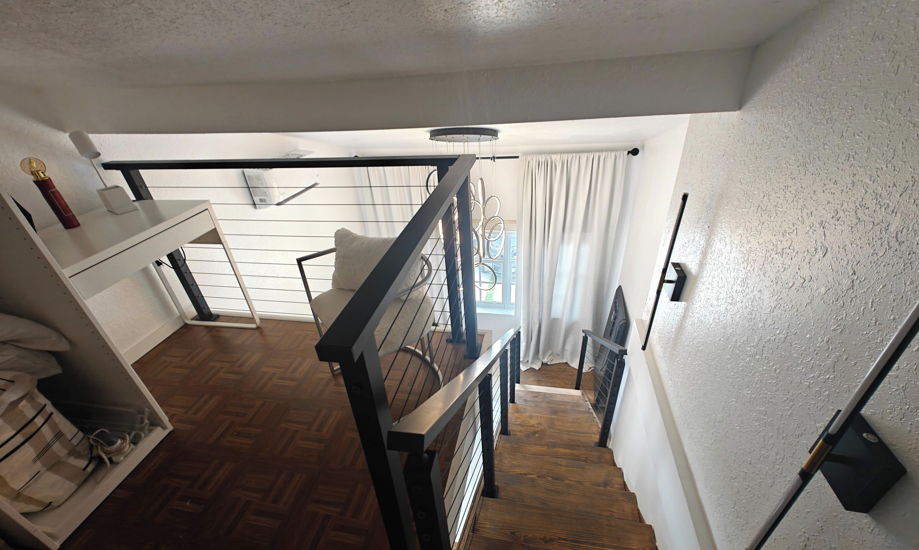 Ein Zimmer mit Holzboden, weißer Wand, schwarzer Geländer und einem mit Vorhängen drapierten Fenster.