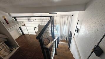 Ein Zimmer mit Holzboden, weißer Wand, schwarzer Geländer und einem mit Vorhängen drapierten Fenster.