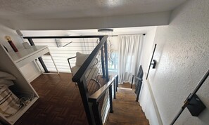 Une pièce avec un plancher en bois, un mur blanc, une rambarde noire et une fenêtre avec des rideaux.