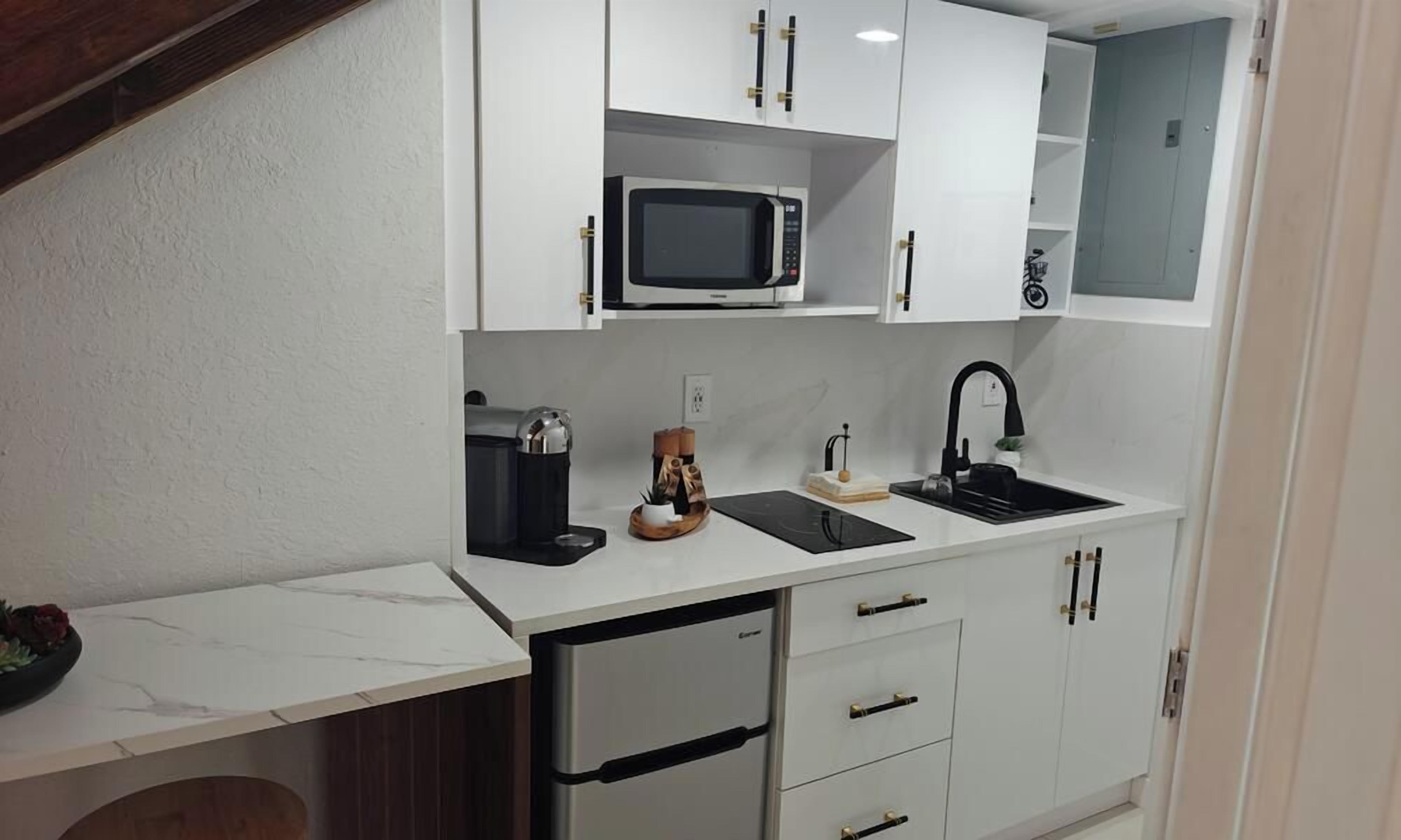 A compact kitchen with white cabinets, a built-in microwave, a coffee maker, and a sink.
