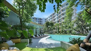 Ein Poolbereich eines Resorts mit Liegestühlen, einem gewundenen Pool und einem modernen Gebäude mit Balkonen.