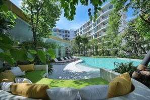 A resort pool area with lounge chairs, a curved pool, and a modern building with balconies. - 2BR Penthouse @ Phyll Phuket next to Central Mall (Tambon Wichit)