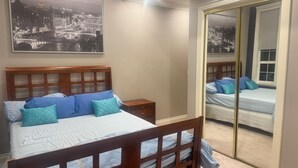 A bedroom with a bed, nightstands, a mirror, and a cityscape painting. - Cozy 1-bedroom private and secured with AC with an independent full bath (Surrey)