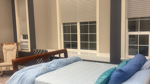 A bedroom with a large bed, two windows with blinds, a chair, and a radiator. - Cozy 1-bedroom private and secured with AC with an independent full bath (Surrey)