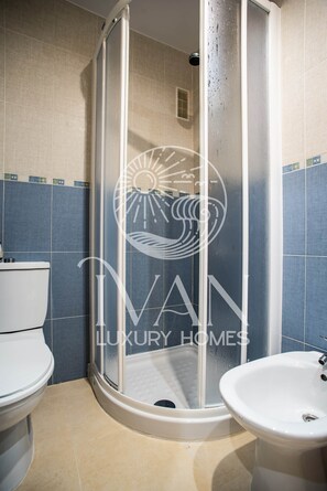 Un baño con ducha acristalada, inodoro y lavamanos.