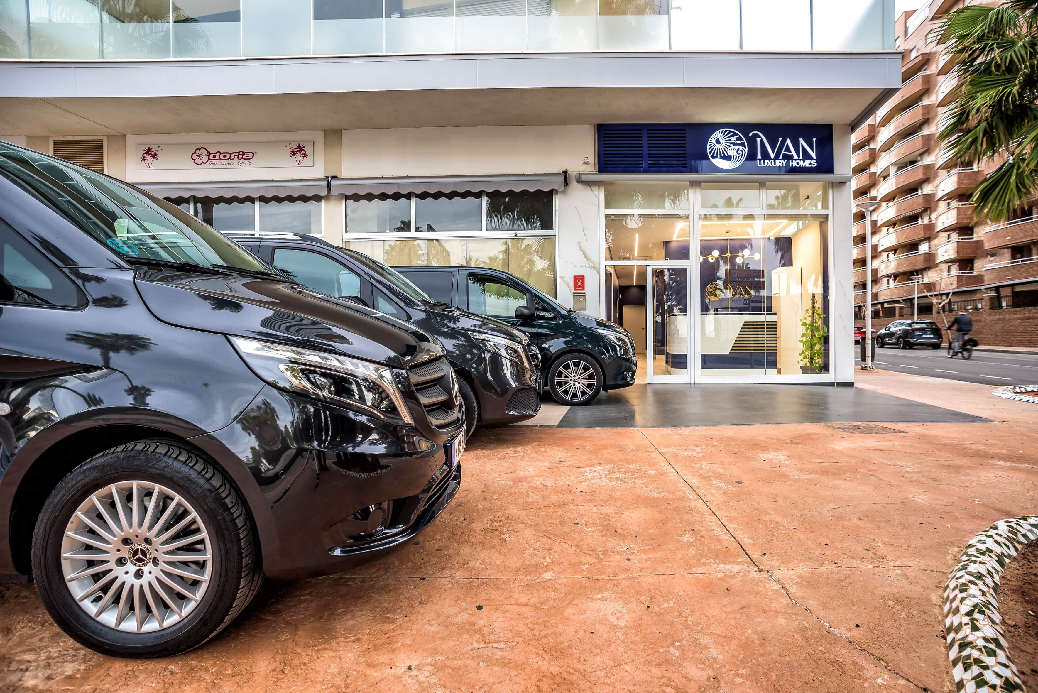 Fila di auto parcheggiate davanti a un edificio con una vetrina che recita 'IVAN LUXURY HOMES'.
