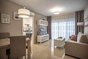 Ein modernes Wohnzimmer mit Essbereich, einem weißen Sofa, einem Couchtisch und einer Küche im Hintergrund.
