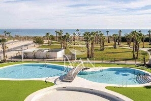 Ein Poolbereich mit Blick auf das Meer, umgeben von Palmen und wolkenlosem Himmel.