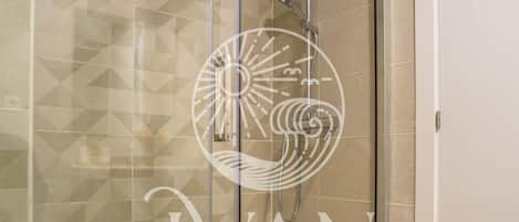 A glass-enclosed shower with a geometric tile pattern on the wall, a white door, and a towel on the floor.