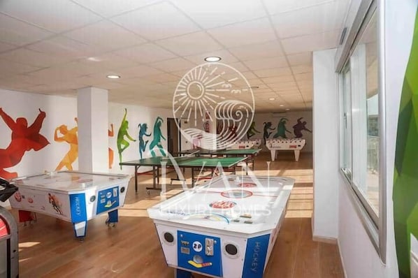 Um ginásio com mesas de futebol de mesa, uma bola de discoteca e murais coloridos nas paredes.