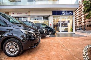 Een rij geparkeerde auto's voor een gebouw met een etalage met de tekst 'IVAN LUXURY HOMES'.