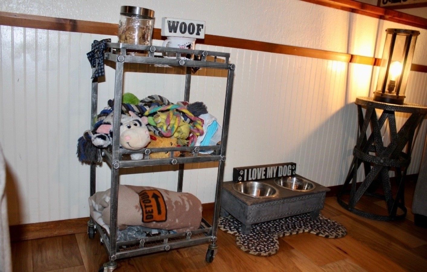 A metal shelf with various plush toys and a 'WOOF' sign, a 'I LOVE MY DOG' sign, and a pet bowl on the floor.