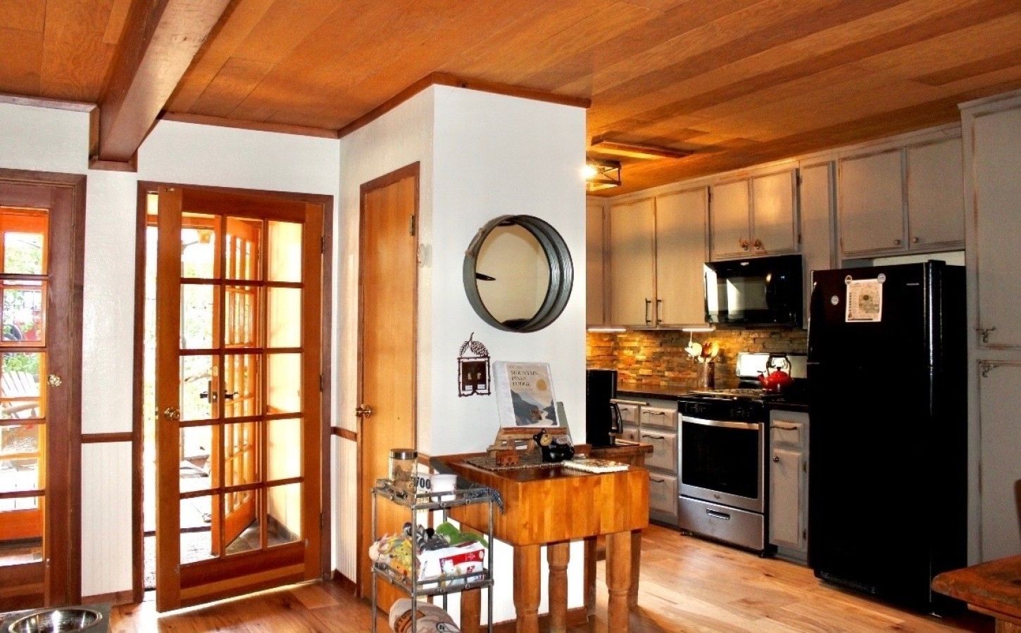 Une cuisine avec des meubles de rangement en bois, un réfrigérateur noir et un coin repas comprenant une table et des chaises en bois.