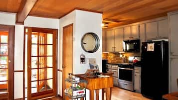 Une cuisine avec des meubles de rangement en bois, un réfrigérateur noir et un coin repas comprenant une table et des chaises en bois.