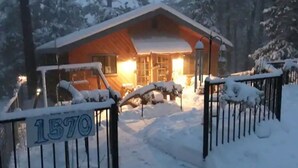 Una cabaña con fachada de madera, una reja metálica con un número y un paisaje cubierto de nieve.