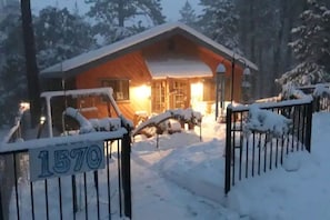 En hytte med træfacade, et metalhegn med et nummer og et sneklædt landskab.