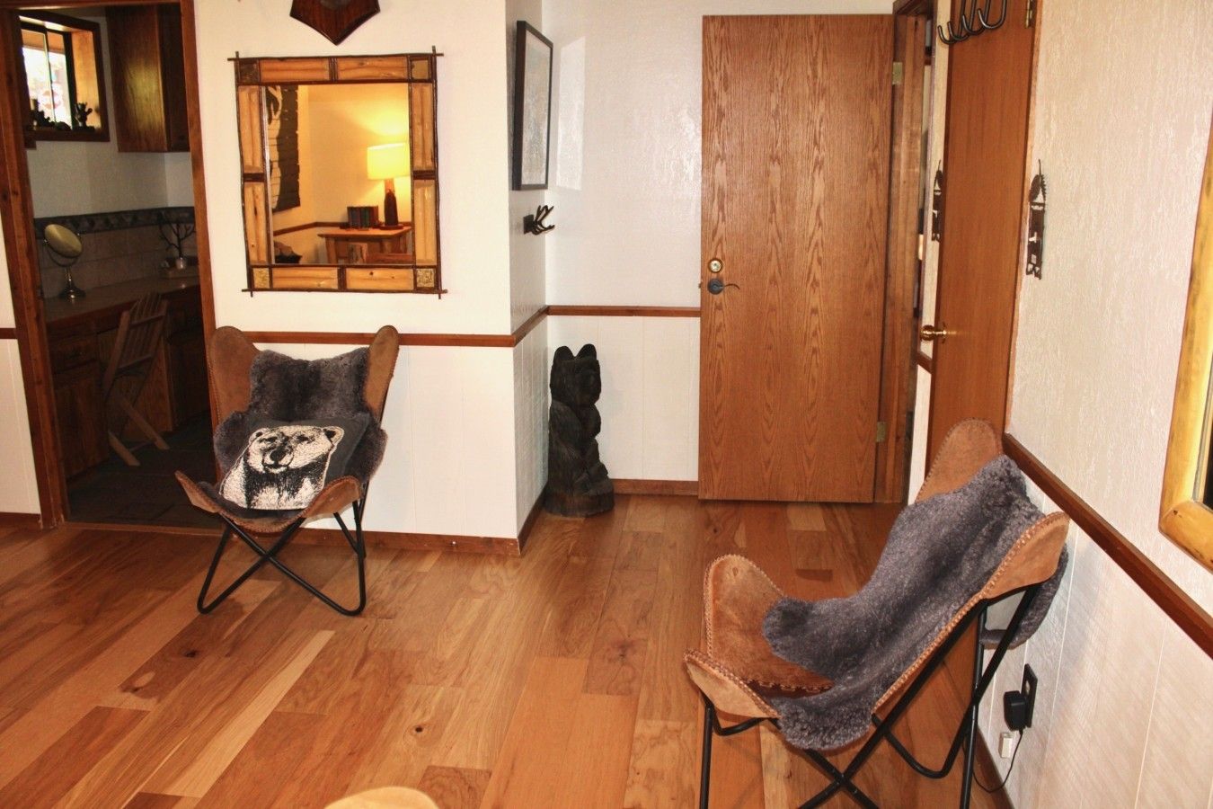 Una habitación con piso de madera, una silla con una manta, una puerta de madera y un espejo en la pared.