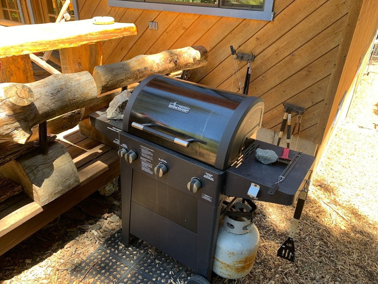 A portable grill with a digital display, a gas tank, and a side table with a brush.