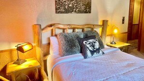 Una cama con cabecera de madera, dos lámparas de noche y un almohadón con diseño de oso.