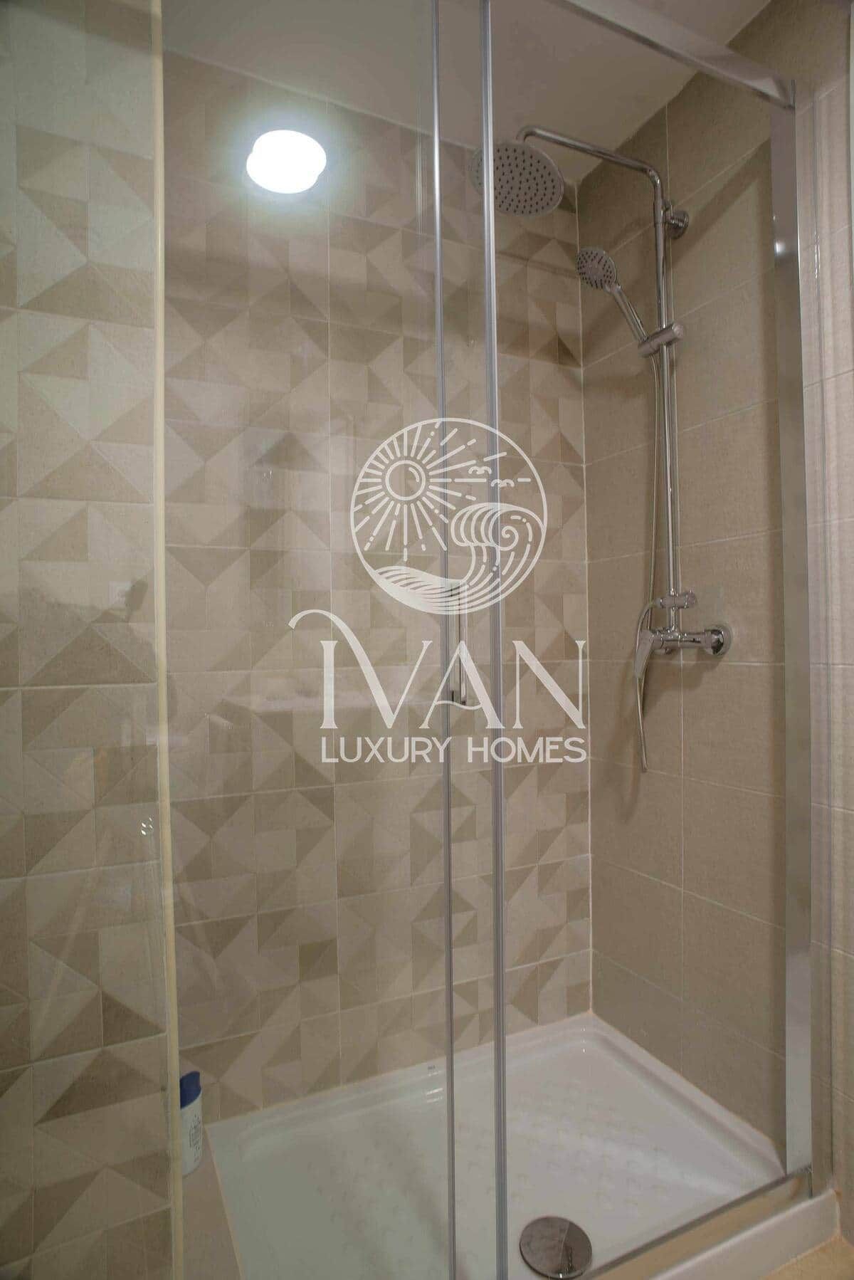 A glass-enclosed shower area with a tiled wall, a showerhead, and a handheld shower attachment.