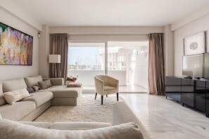 A modern living room with a sectional sofa, a single armchair, a flat-screen TV, and a large window with a view of the city. - Cosy Apartment inside Puerto Marina, steps to the Sea (Benalmádena)