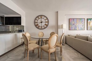 A modern living room with a round dining table, beige chairs, a large wall clock, abstract paintings, and a sofa. - Cosy Apartment inside Puerto Marina, steps to the Sea (Benalmádena)