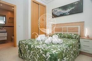A hotel room with a bed, a nightstand, a bedside table, a wall-mounted TV, and a bathroom visible through an open door. - Casa Alegria Ivan Luxury Homes, 10th Floor South, 1st Line (Oropesa del Mar)