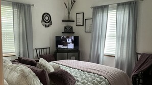 Un dormitorio con cama, televisión y cortinas.