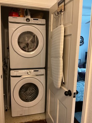 Una lavanderia con due lavatrici affiancate, uno stendibiancheria e una porta che dà su una camera da letto.