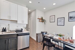 A modern kitchen with stainless steel appliances, white cabinetry, and a dining area with a table set for two. - Family-Friendly 3BR/3.5BA in Fairmount near Center City Philadelphia (Philadelphia)