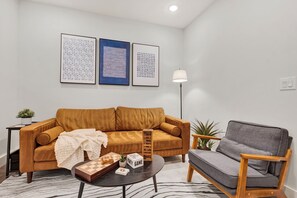 A living room with a brown sofa, a gray armchair, a coffee table, and a floor lamp. There are three framed artworks on the wall. - Family-Friendly 3BR/3.5BA in Fairmount near Center City Philadelphia (Philadelphia)