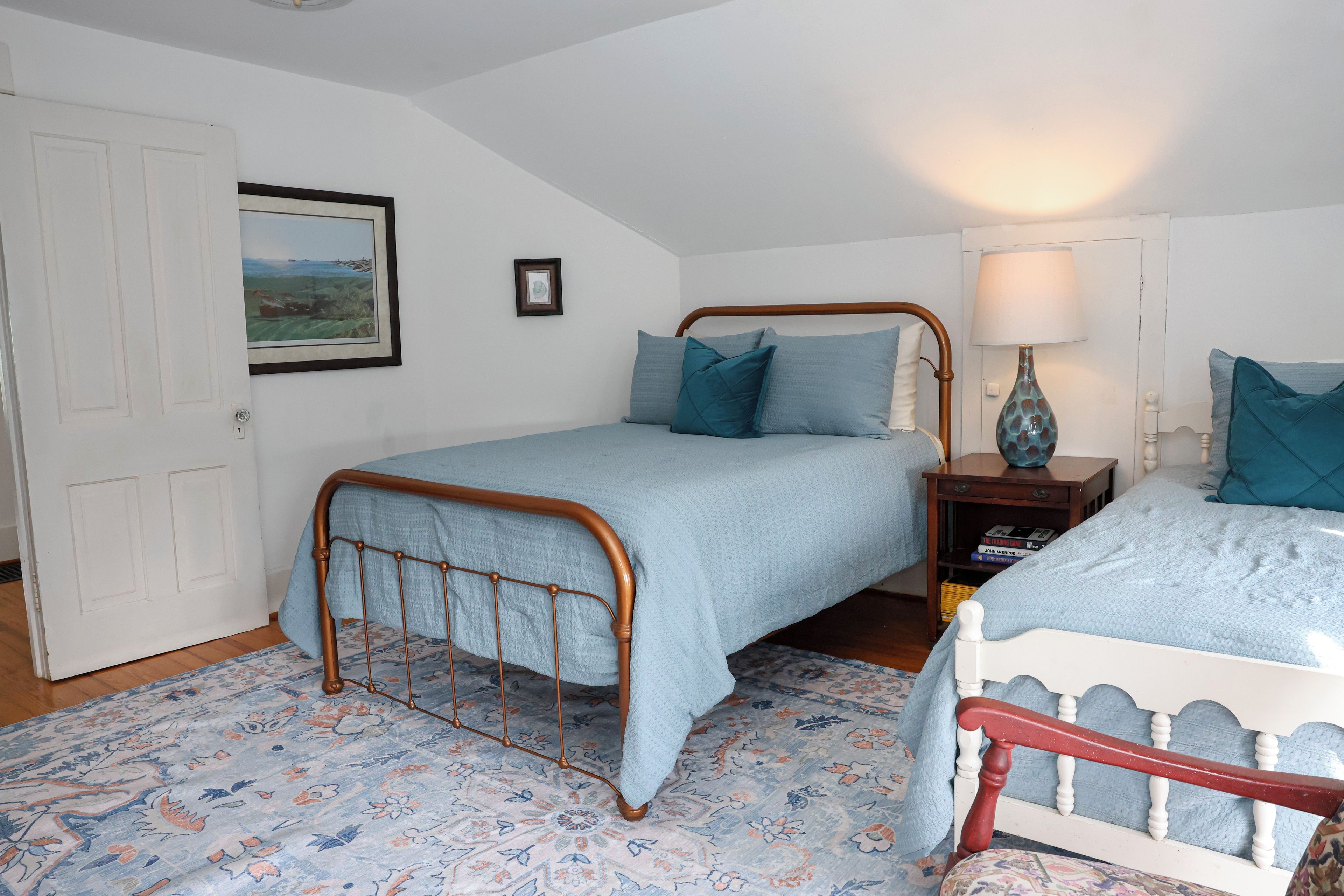 A bedroom with two single beds, a nightstand with a lamp, a framed picture on the wall, and a patterned carpet.