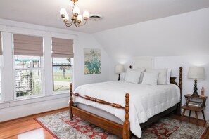 A bedroom with a wooden four-poster bed, a chandelier, a window with blinds, and a view of the outside. - Spacious 3 bed 2 1/2 bath home on Palacios waterfront. Great views and location. (Palacios)