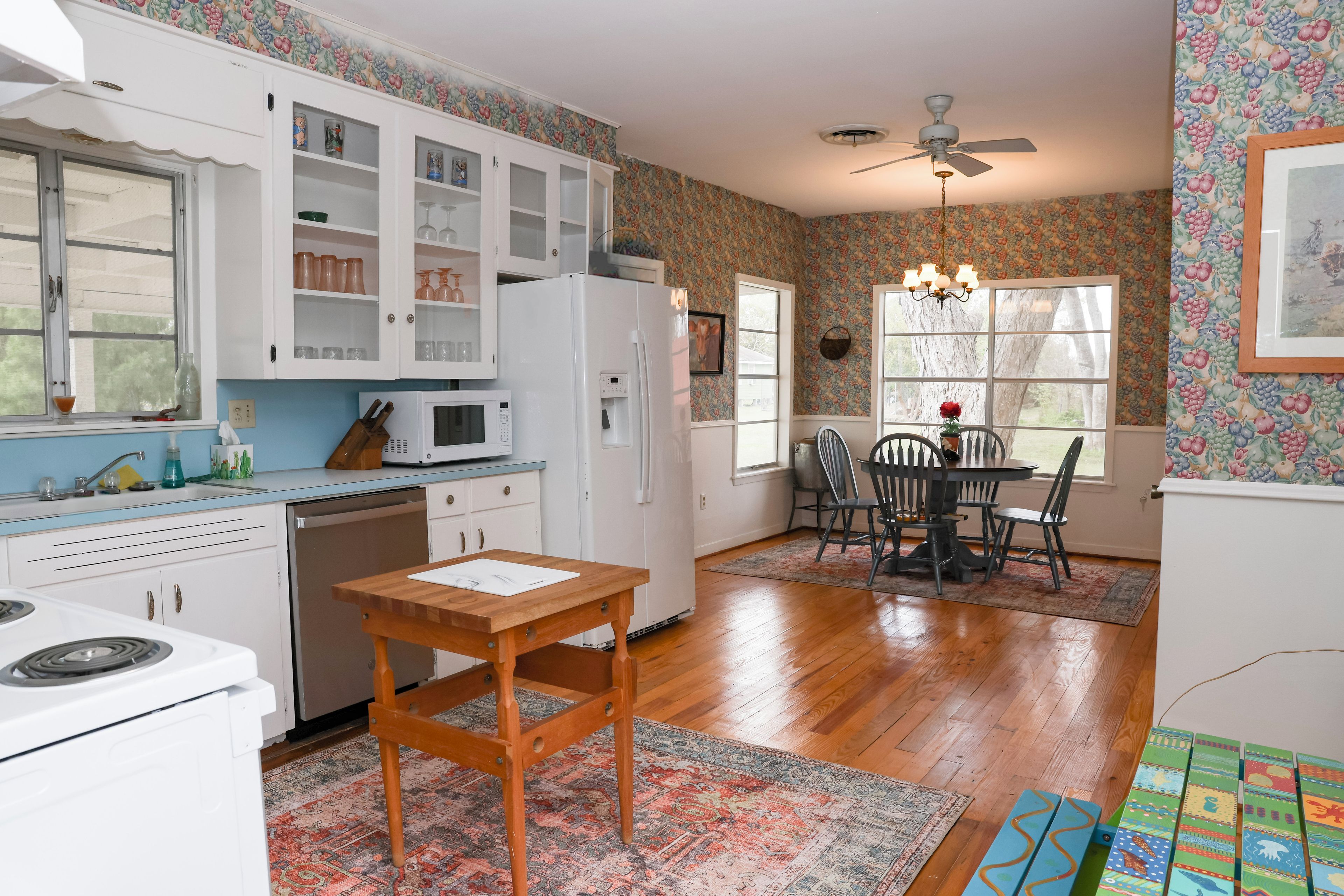 A kitchen with white cabinets, a microwave, a refrigerator, and a dining area with a table and chairs.
