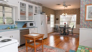 A kitchen with white cabinets, a microwave, a refrigerator, and a dining area with a table and chairs.