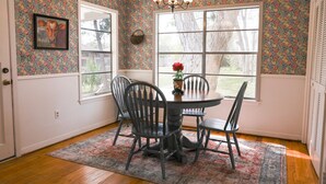 Un comedor con una mesa y sillas, una araña y un ventanal con vista a árboles.