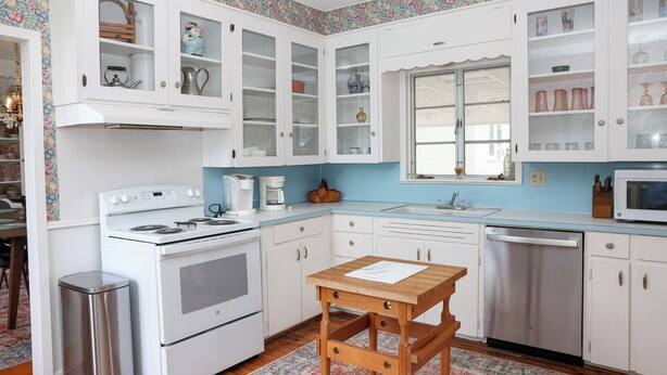 Una cocina con armarios blancos, una estufa, un fregadero y un microondas.
