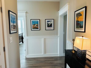 En hall med inramade bilder av Paris, Strasbourg och Louisasjön, en vit panelvägg och en lampa på ett bord.