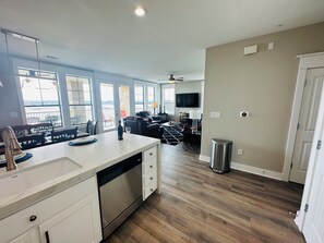 A modern kitchen with a dishwasher, a dining area with a table and chairs, and a living room with a sofa and a TV. - Lake Travis Water Front - 180' Water Views  -3 beds and two baths (Jonestown)