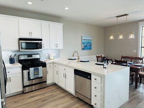 A modern kitchen with white cabinetry, stainless steel appliances, and a wooden dining area. - Lake Travis Water Front - 180' Water Views  -3 beds and two baths (Jonestown)