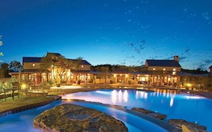 A large outdoor swimming pool with a stone border, surrounded by a building with multiple rooms and a covered patio area. - Lake Travis Water Front - 180' Water Views  -3 beds and two baths (Jonestown)