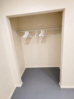 A closet with a grey floor and white walls, featuring a metal rod with white hangers.
