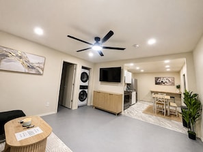 A modern living space with a ceiling fan, a flat-screen TV, a dining area, and a kitchen.