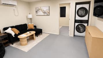 Un espace de vie compact comprenant un canapé, une table basse et un lave-linge placé dans un coin.
