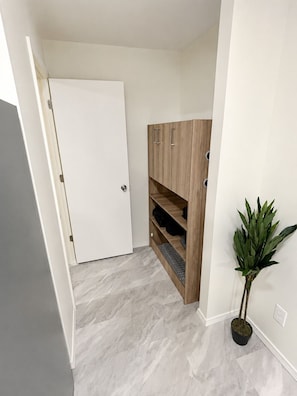 A hallway with a white door, a wooden wardrobe with shelves, and a potted plant.
