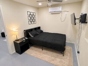Een slaapkamer met een bed, bedlampje, airconditioning en een plafondventilator.