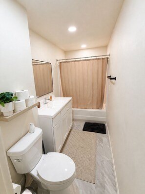 Een badkamer met toilet, wastafel, spiegel, douchegordijn en een kleine potplant.