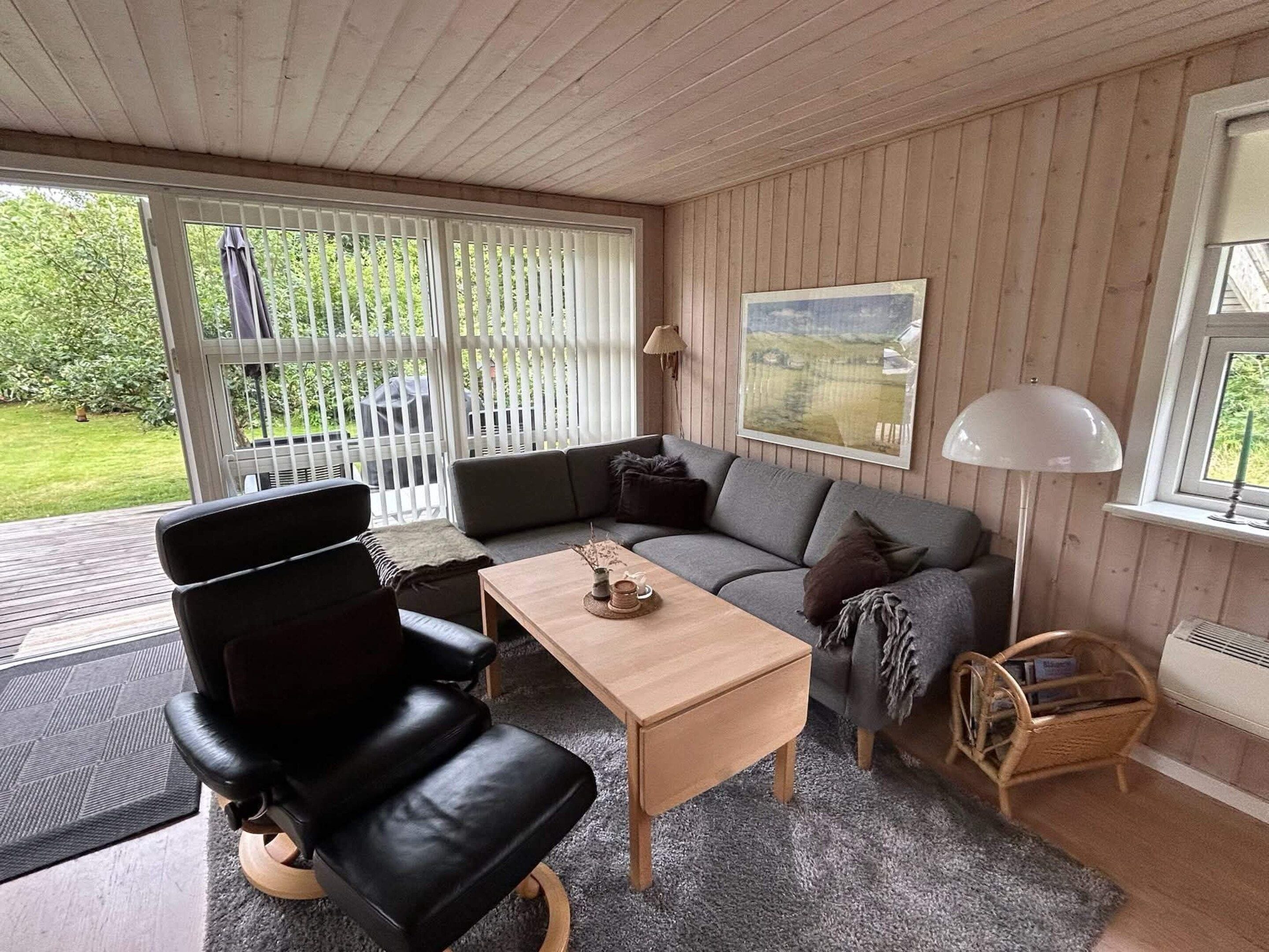A cozy living room with a black leather chair, a grey sofa, a wooden coffee table, and a wicker side table.