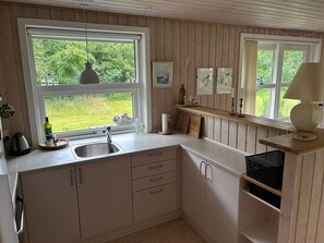 Una cocina con paneles de madera, un lavamanos, una ventana con vistas a zonas verdes y una estantería con una lámpara.