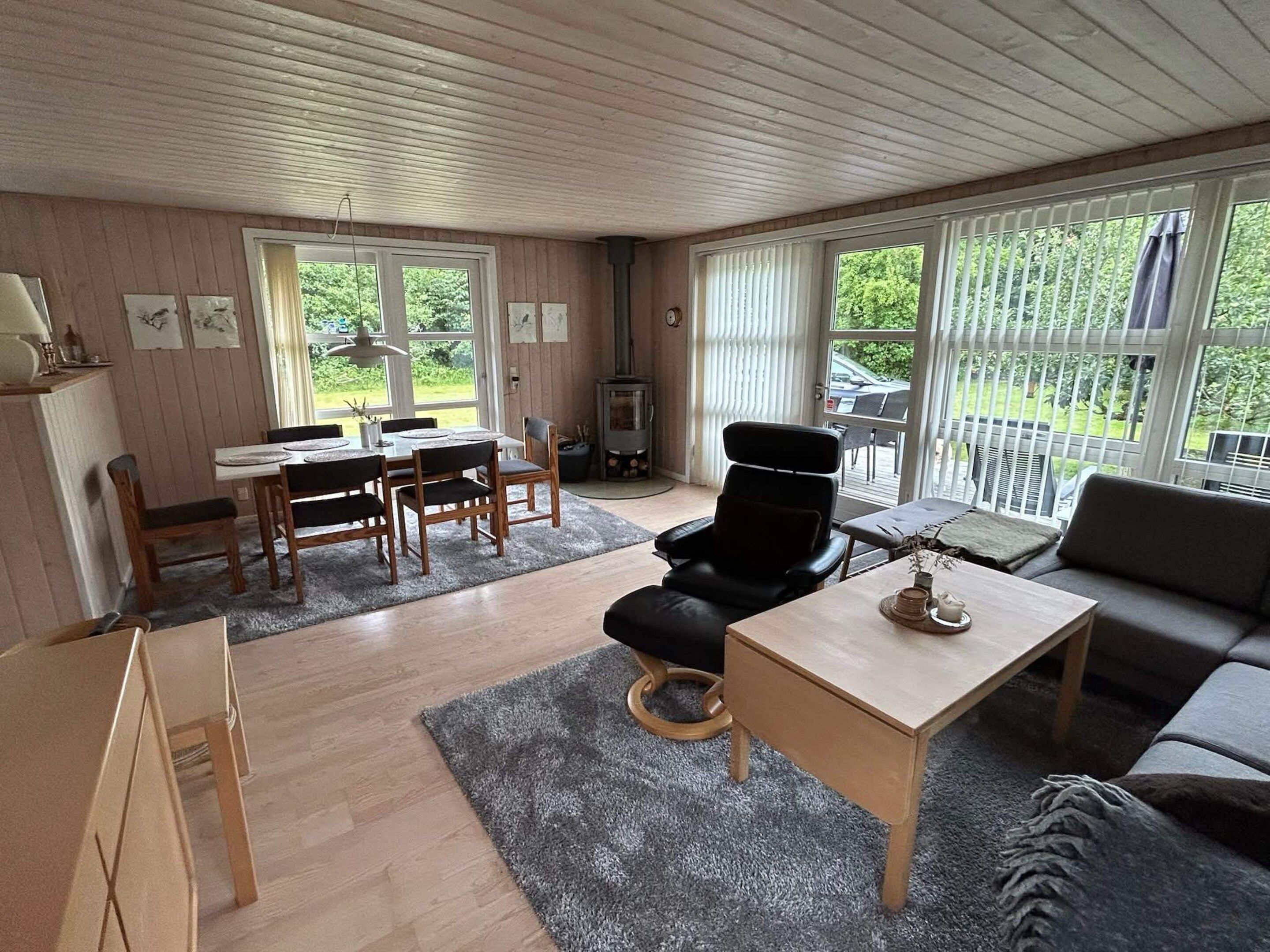 A room with a dining table, chairs, a sofa, a small table with a lamp, and a fireplace.